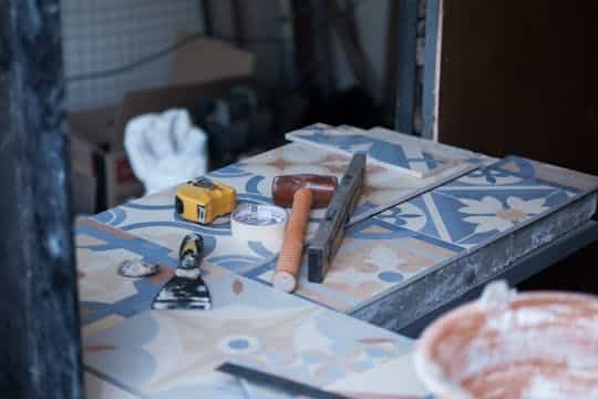 Flooring Cincinnati Tools and tiles on a construction site, ready for tiling work. Includes trowel, tape measure, and adhesive tape.